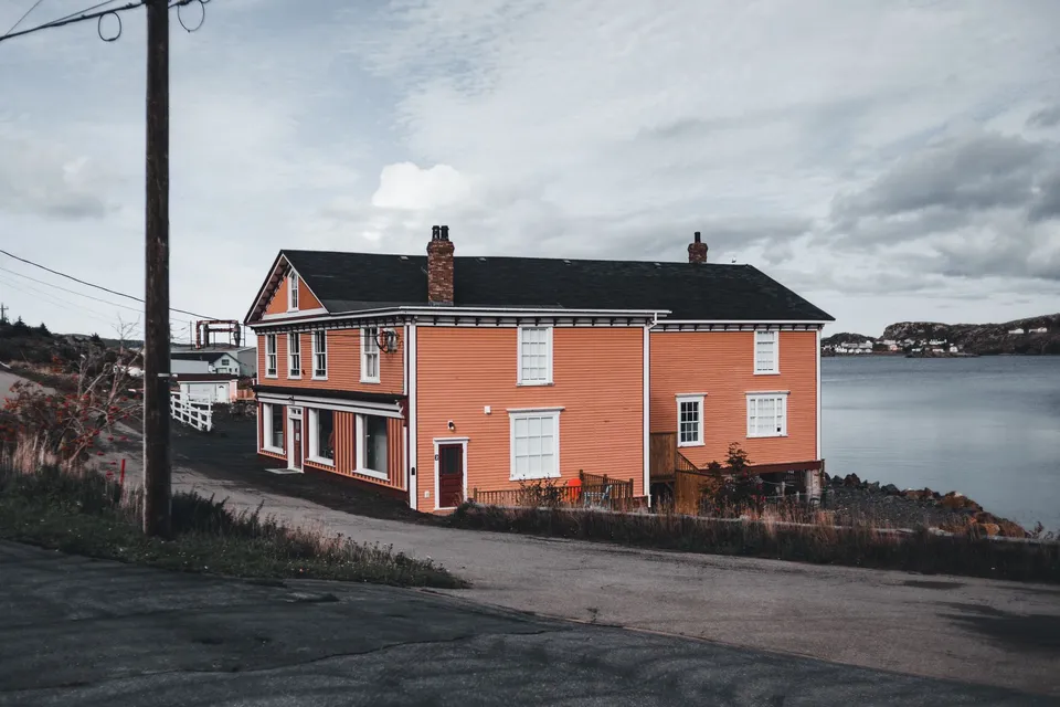 Orange wooden house by a serene lake under a cloudy sky in a small town setting.