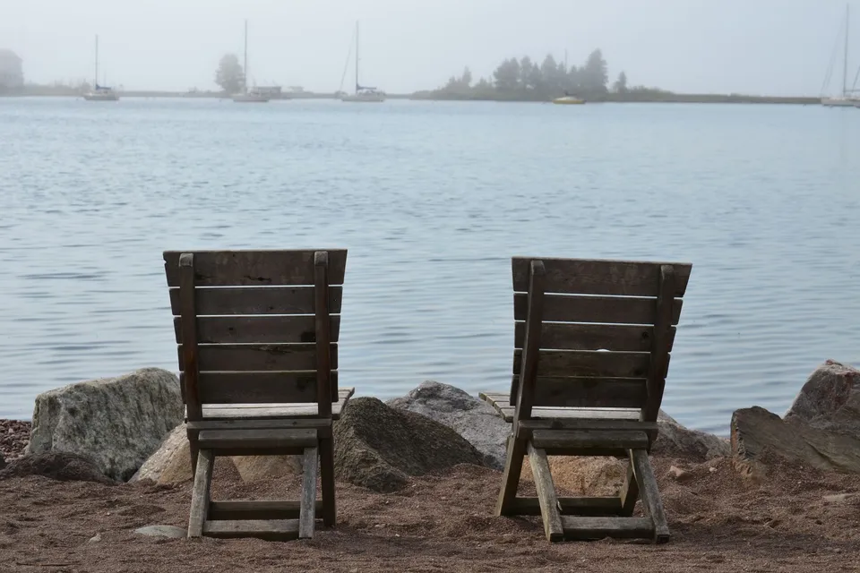Two wooden chairs on a sandy beach in Grand Marais, MN, offering a peaceful view over a calm lake.